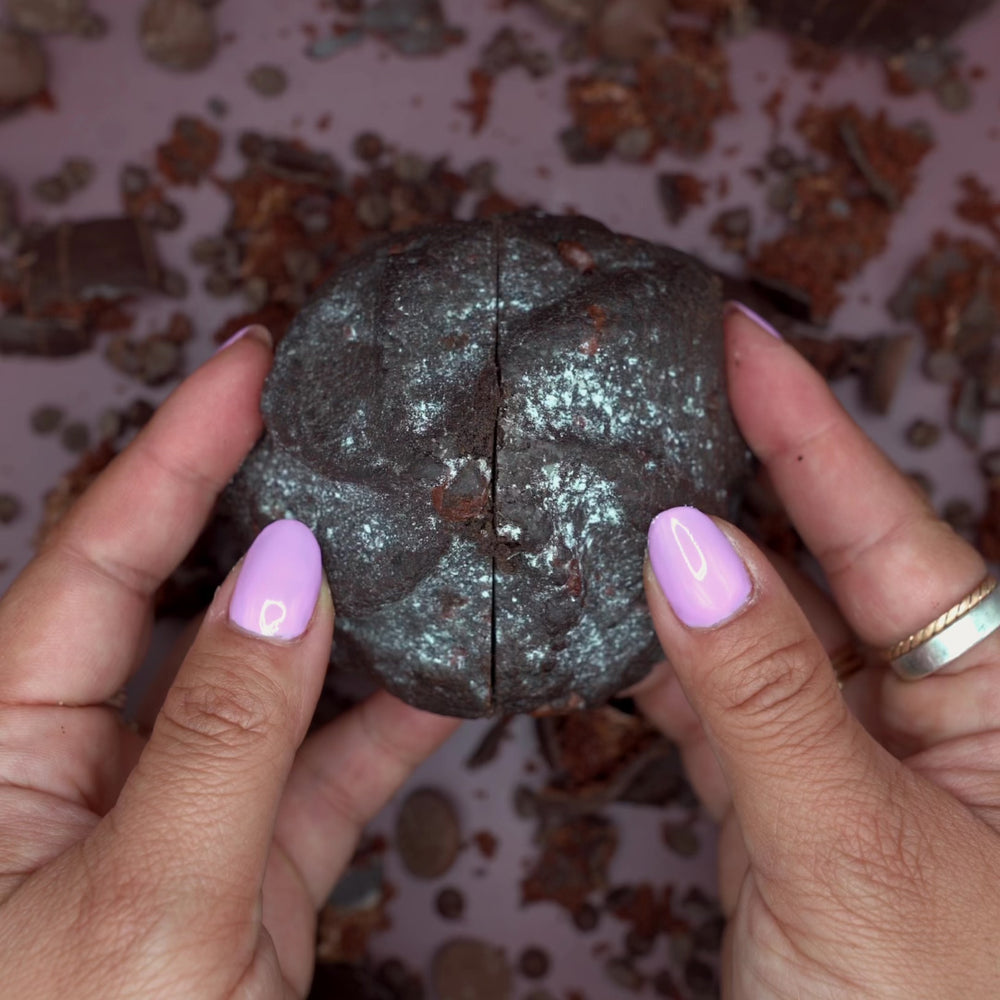 Hands breaking a Massive Eruption chocolate cookie revealing gooey fudge center