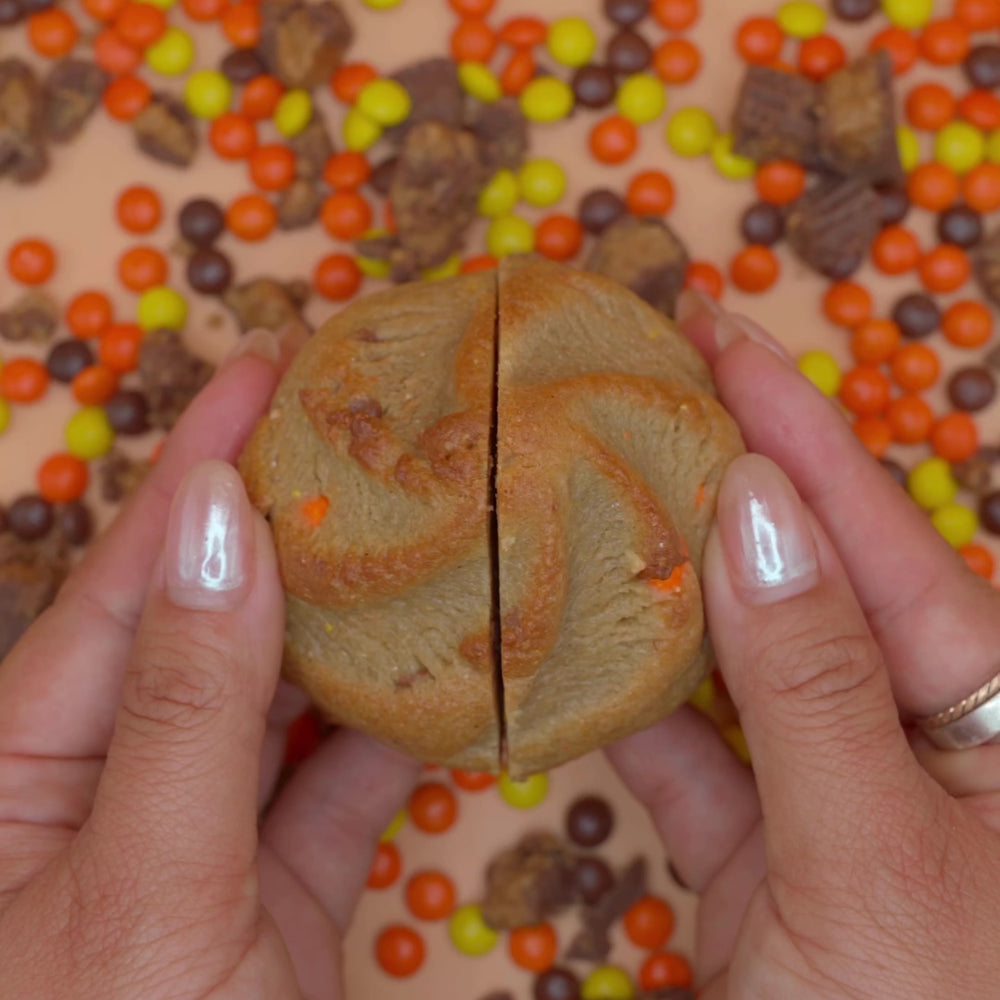 Hands splitting a Pudge cookie to show its rich chocolate and peanut butter core