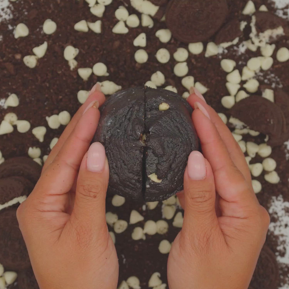 Hands pulling apart a Black Beauty black cocoa cookie to show its creamy cookies and cream frosting center