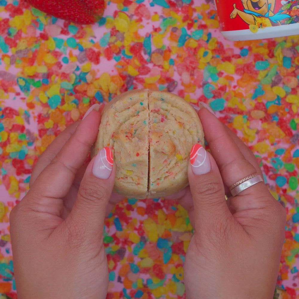 Hands breaking open fruity cereal stuffed cookie revealing the creamy fruity frosting center