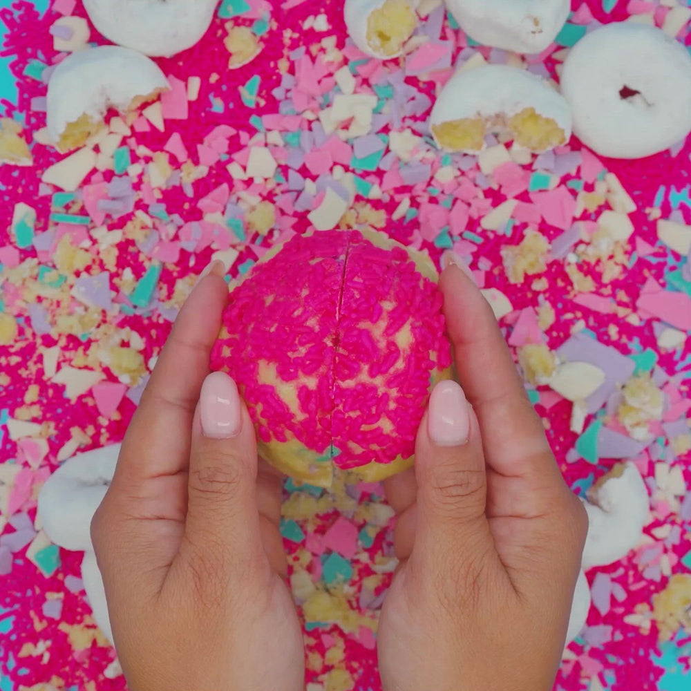Hands breaking open stuffed Sugar Cookie with pink sprinkle donut center