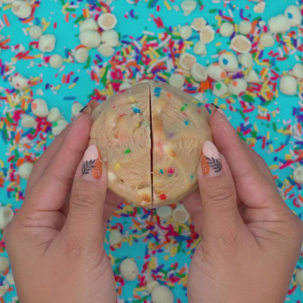 Hands pulling apart a Caked Up confetti cookie revealing pink cake pop center