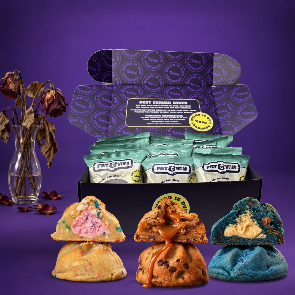 An open Fat & Weird box of wrapped cookies with stuffed cookies cut open in front, next to a vase of dead roses